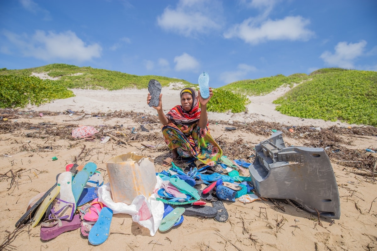 Woman sitting on a beach with a bounty of discarded colorful flip-flops in front of her